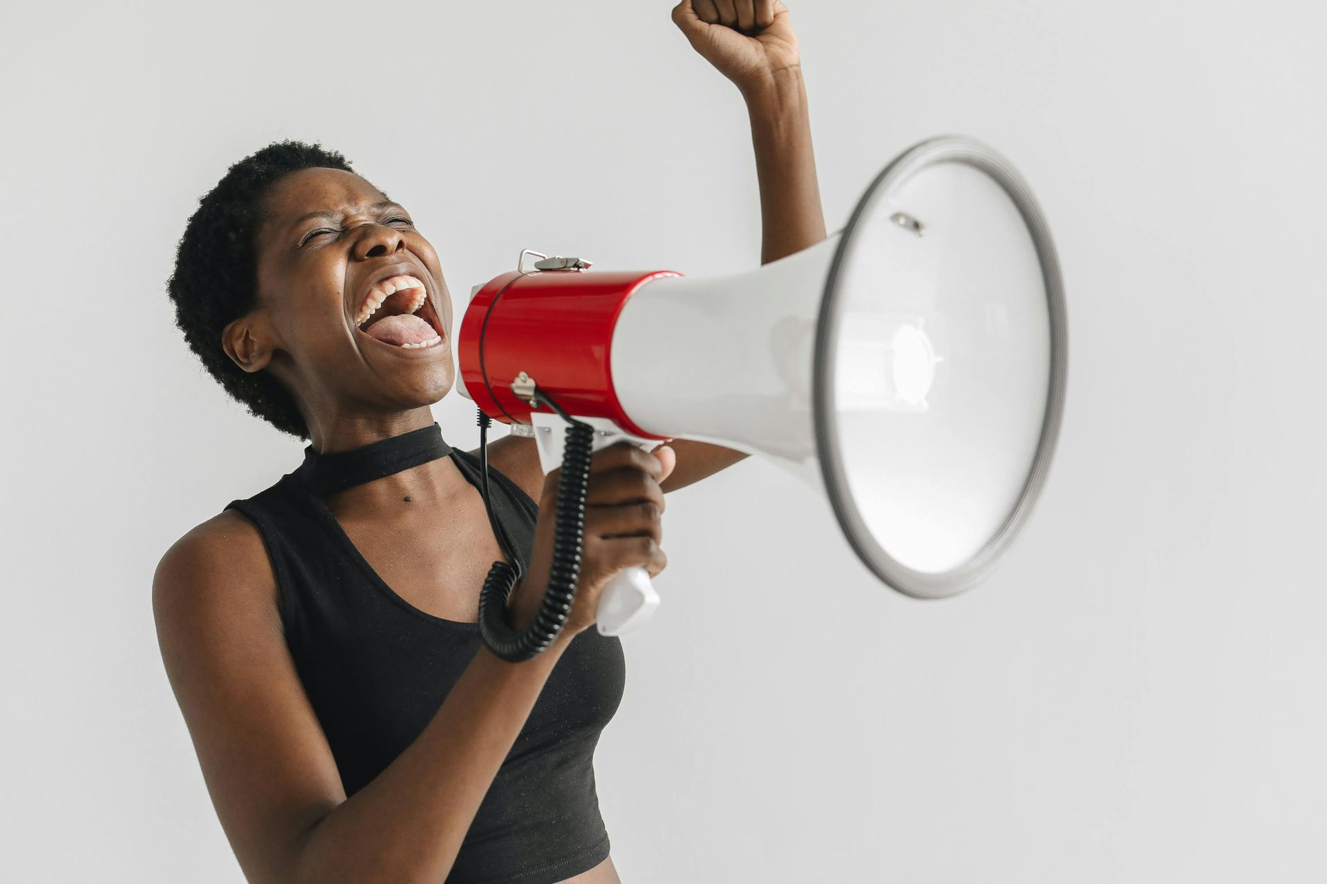 Woman with short hair yelling into a red and white megaphone, arm raised in a gesture of protest.