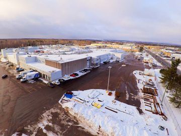 Aerial view of a large warehouse complex with snow-covered roofs and grounds under a bright winter sky.