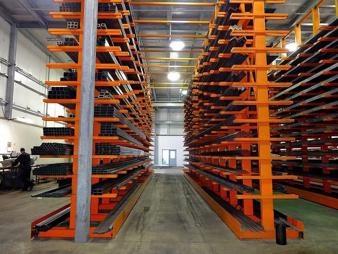 Warehouse interior with rows of tall, orange industrial cantilever shelving holding metal materials.