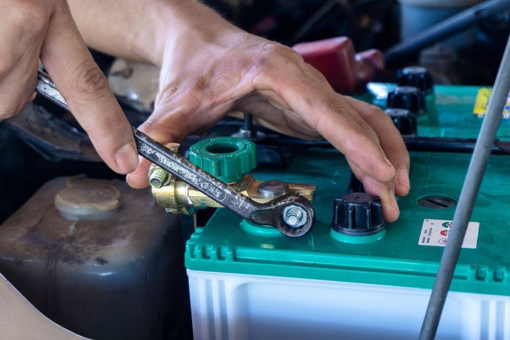 A Person Is Working On A Car Battery With A Wrench — Coastal Farm & Motorcycles In Atherton, QLD