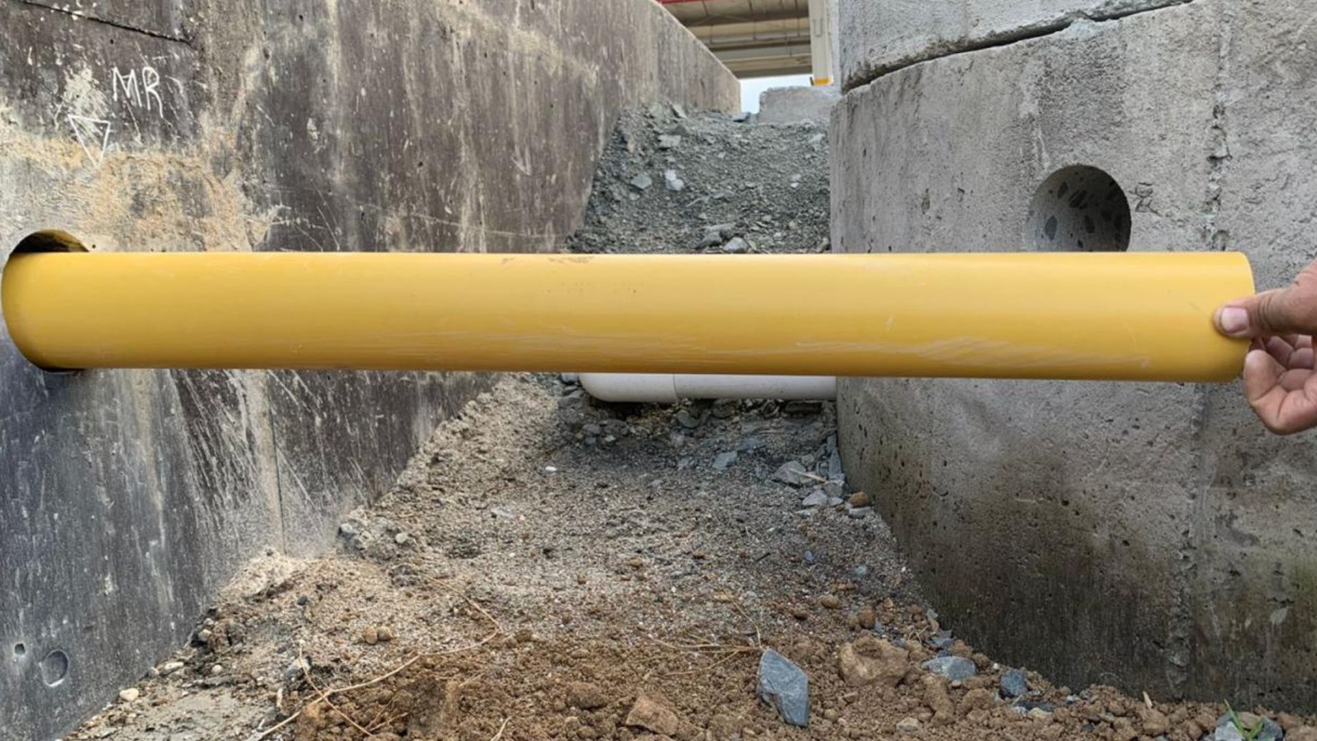 Una persona sostiene un tubo amarillo frente a una pared de hormigón.