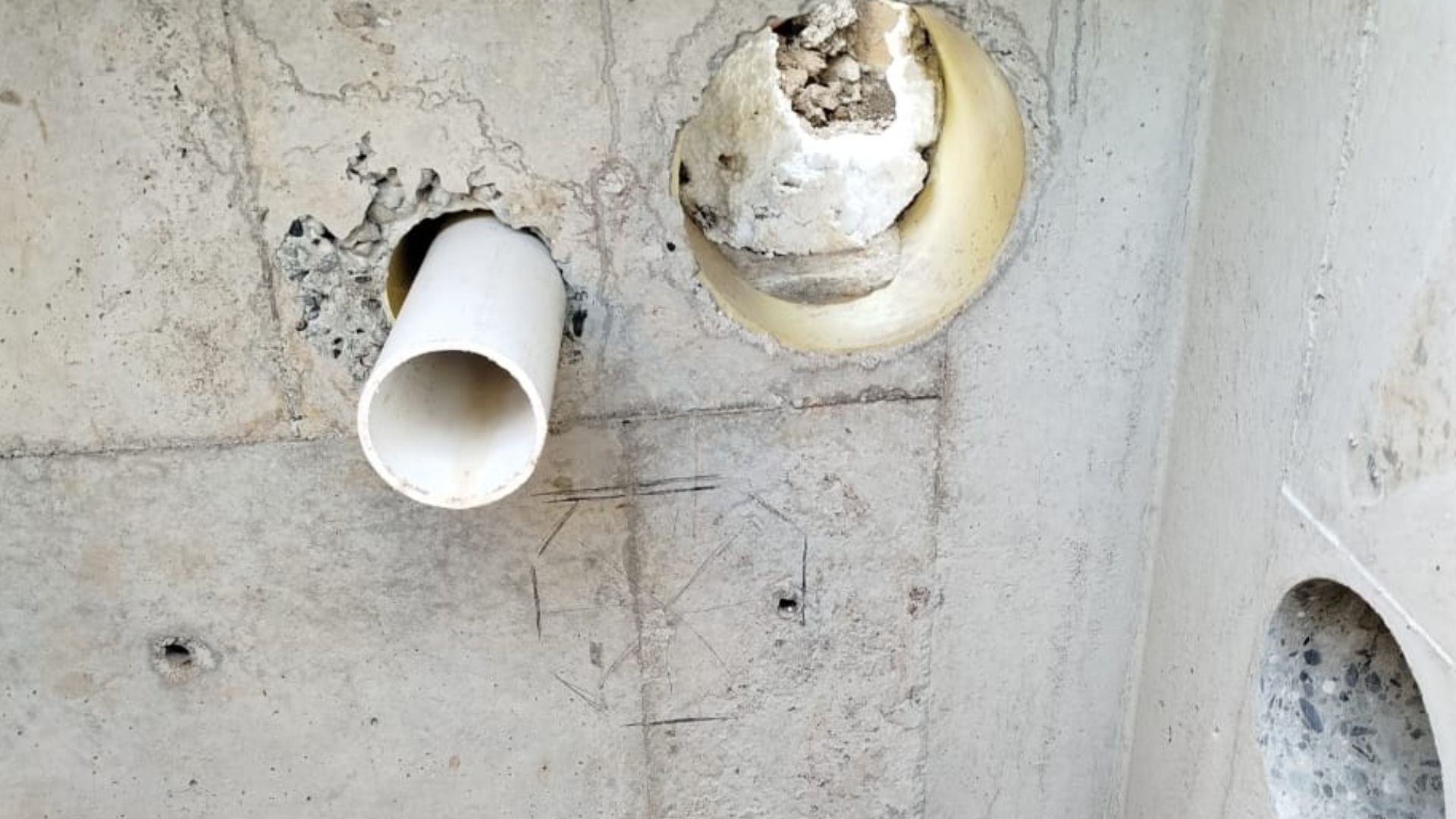 Un tubo blanco sale de un agujero en una pared de hormigón.