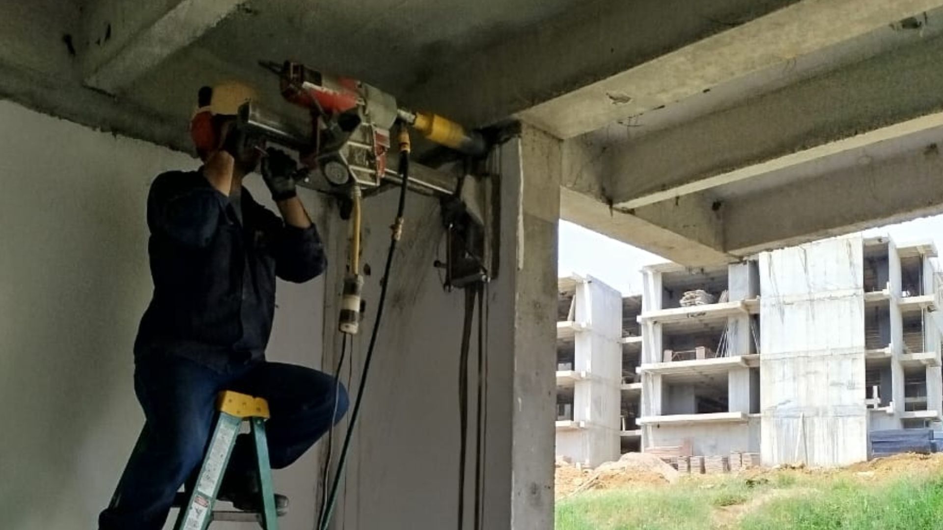 Un hombre está sentado en una escalera usando una máquina para cortar un agujero en una pared de hormigón.