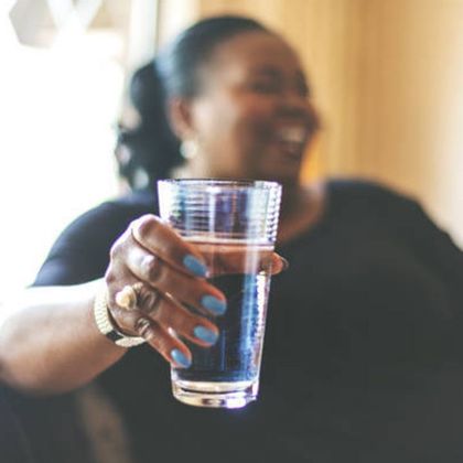 A woman with blue nails is holding a glass of water