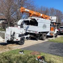 A tree chipper truck is parked in a driveway next to a stihl chainsaw.