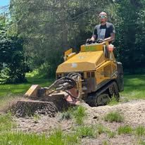 A man is driving a stump grinder in a yard.