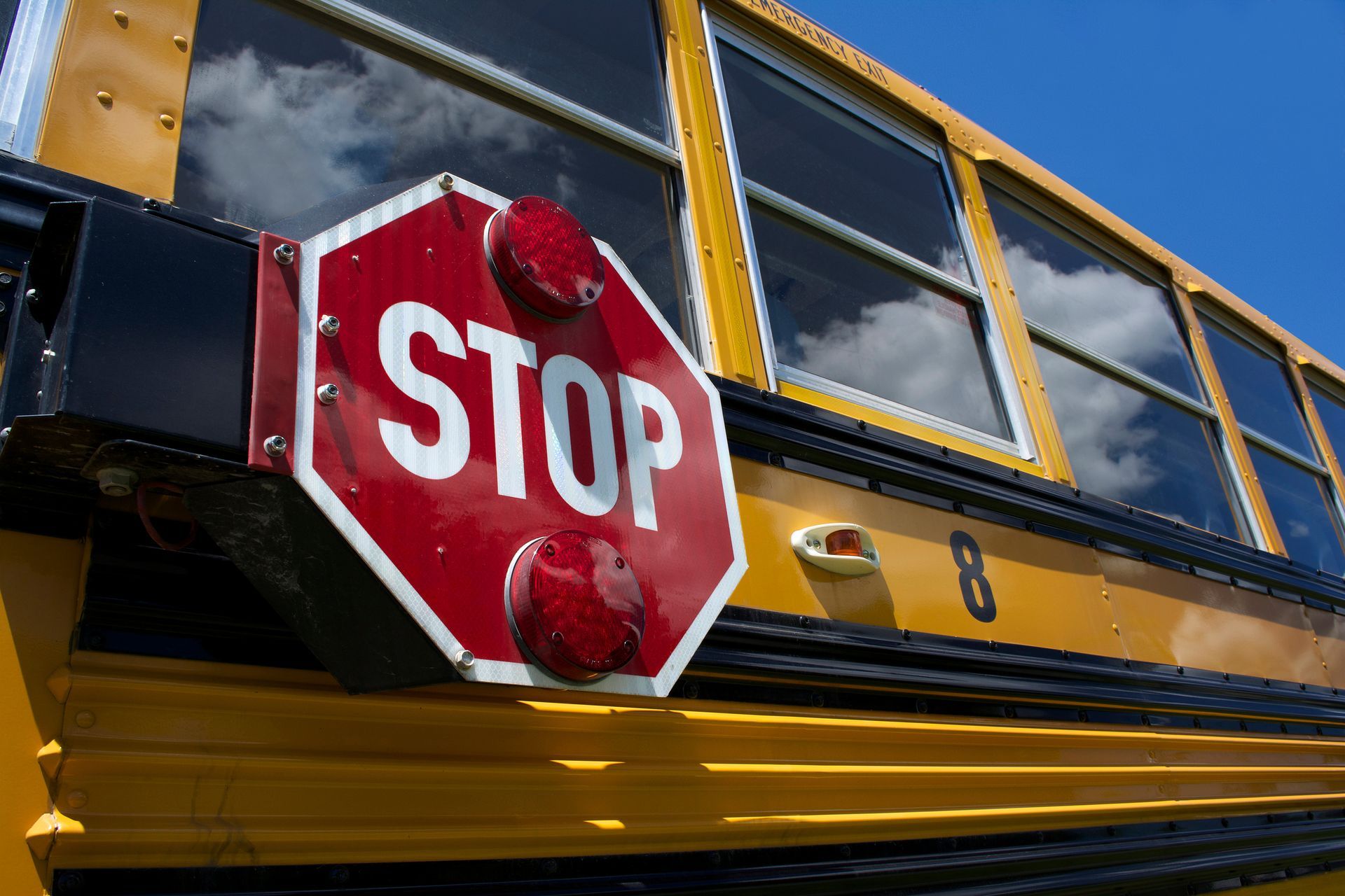Yellow school bus, red stop sign extended with flashing lights, against a blue sky.