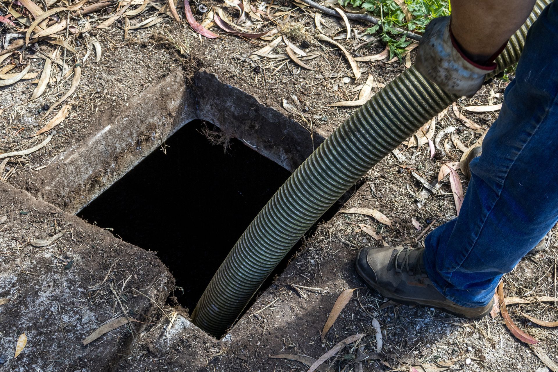 Worker inserting hose into septic tank for pumping service. 