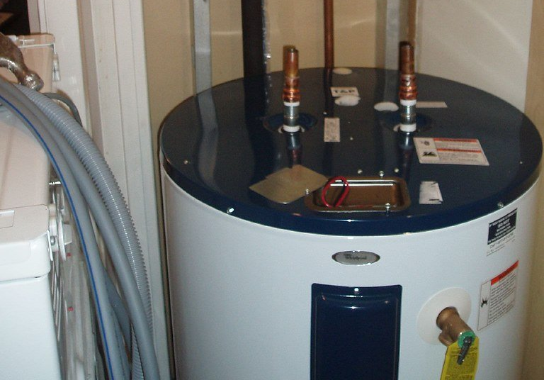 A white and blue water heater is sitting next to a washer and dryer.