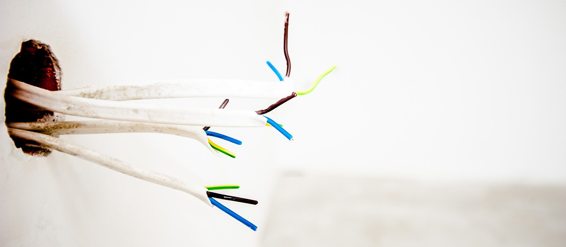 A bunch of wires are coming out of a hole in a wall.