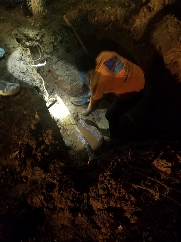 A person is digging in the dirt with a flashlight.