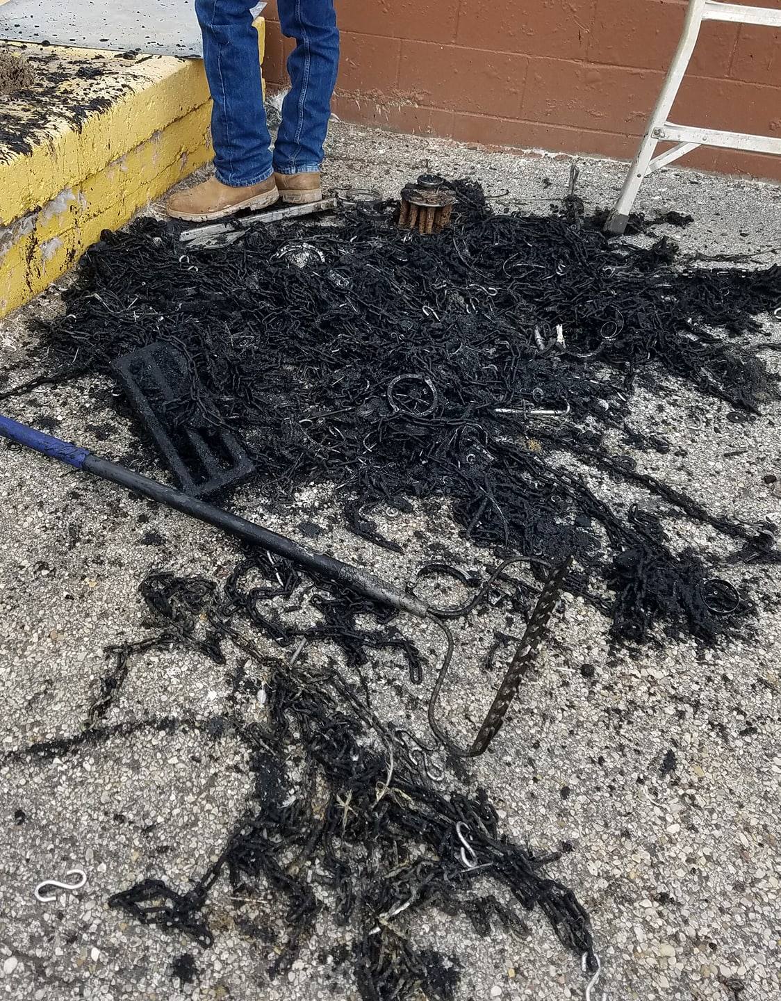 A person is standing next to a pile of black shavings on the ground.