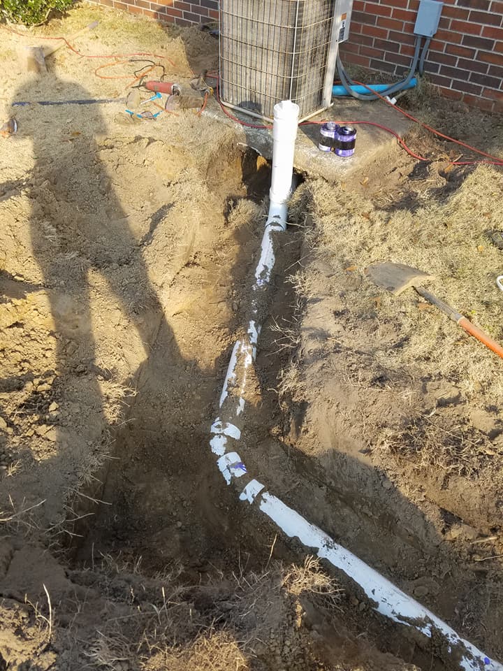 A pipe is being installed in the dirt next to a brick building.