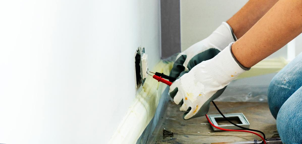 A person is using a multimeter to test an electrical outlet.