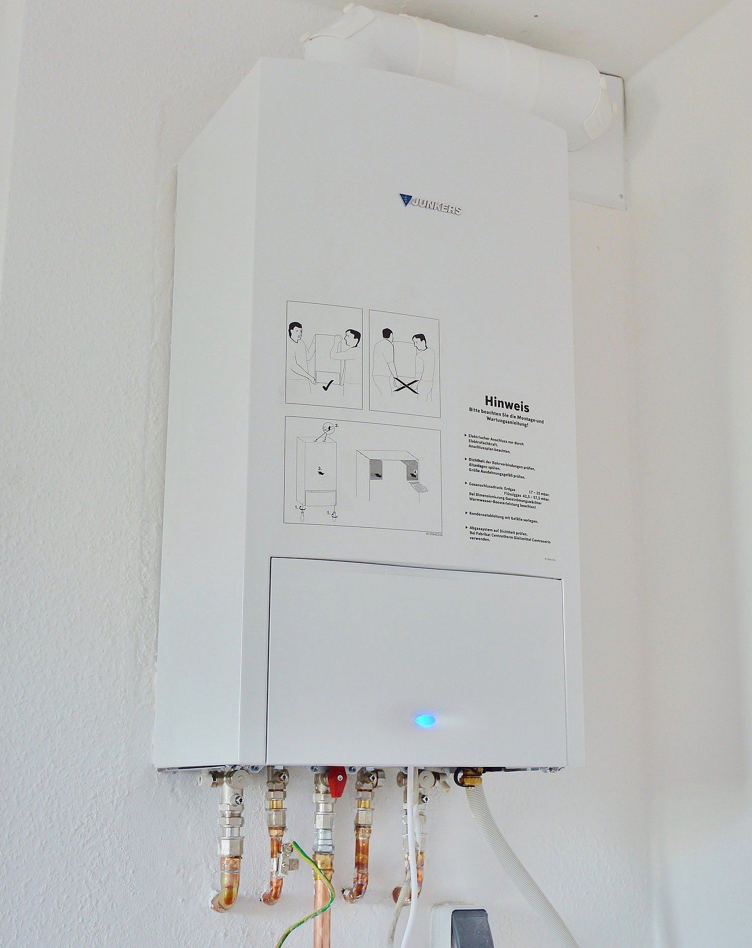 A white boiler is hanging on a white wall.