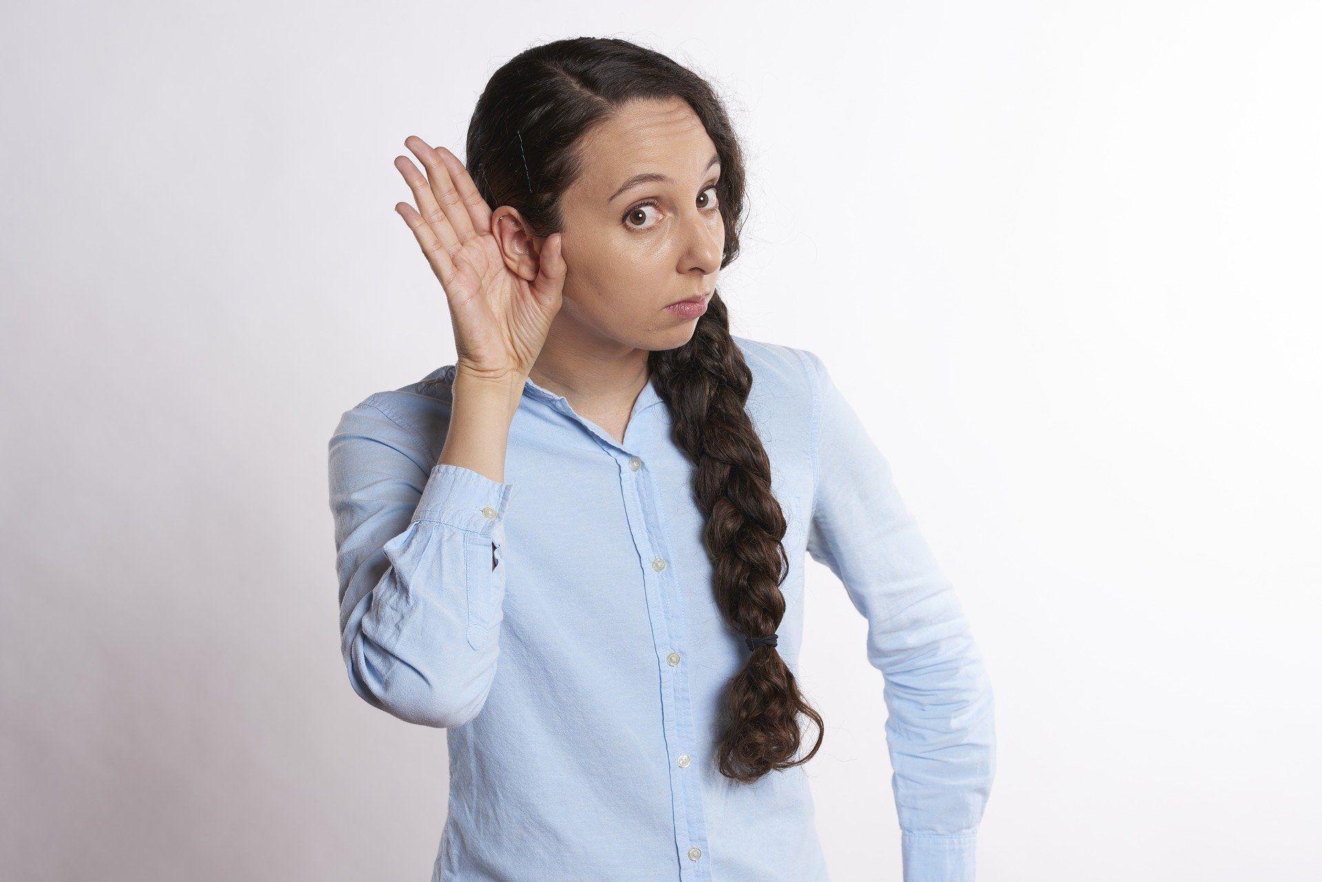 A woman is listening to something with her hand to her ear.