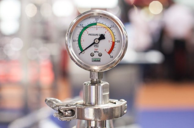 A pressure gauge is sitting on top of a stainless steel pipe.