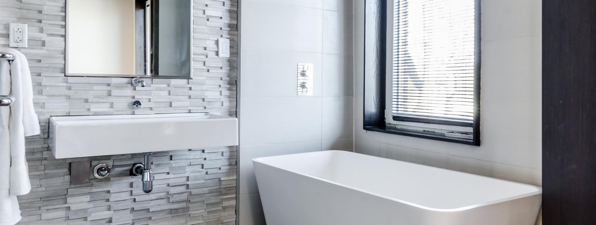 A bathroom with a tub , sink , mirror and window.