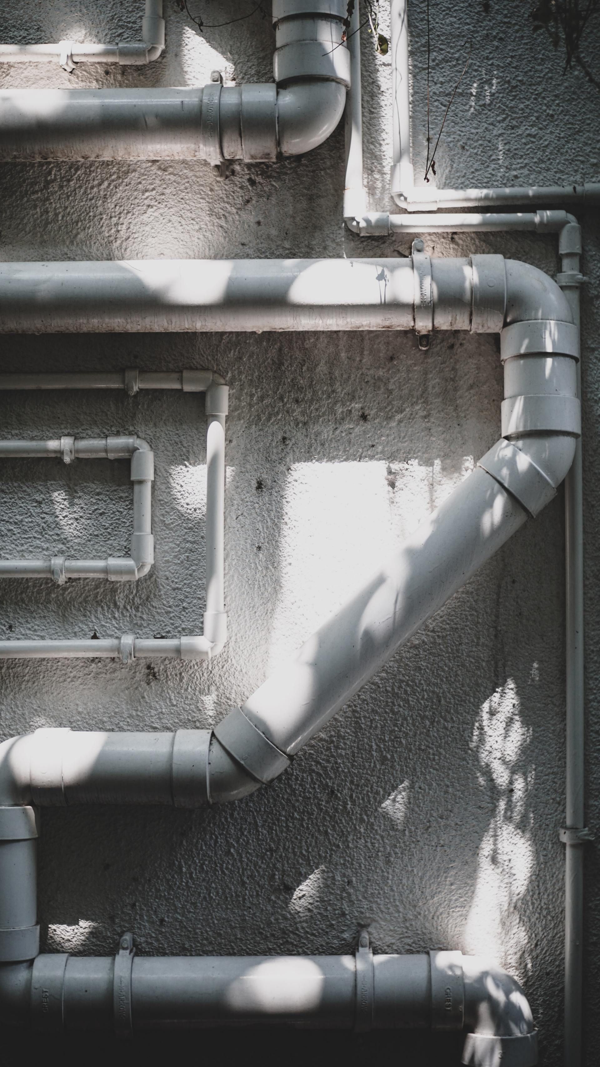 Gray metal pipes on a textured wall with sunlight casting diagonal shadows