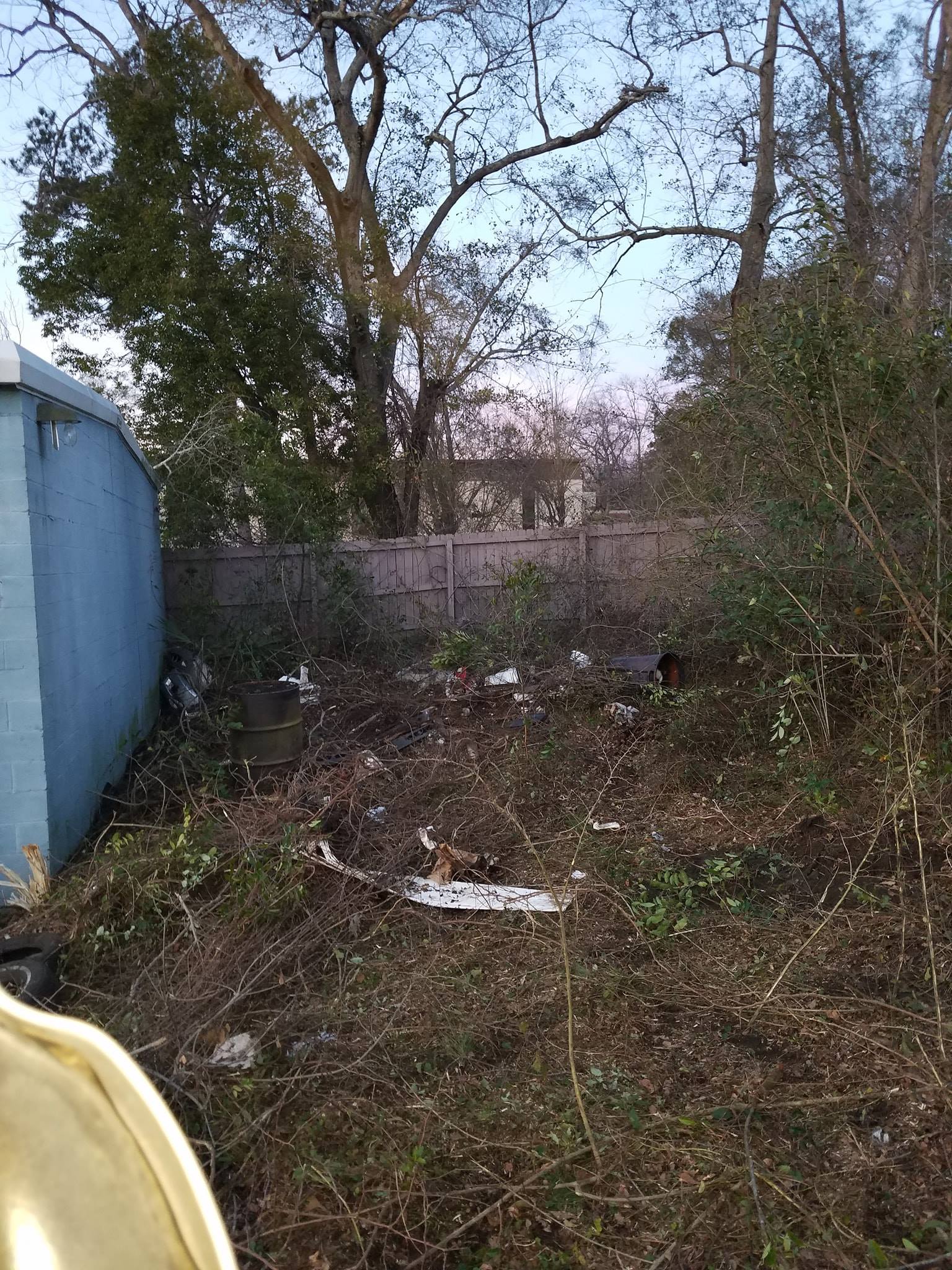 A dirty yard with a blue building in the background and trees in the background.