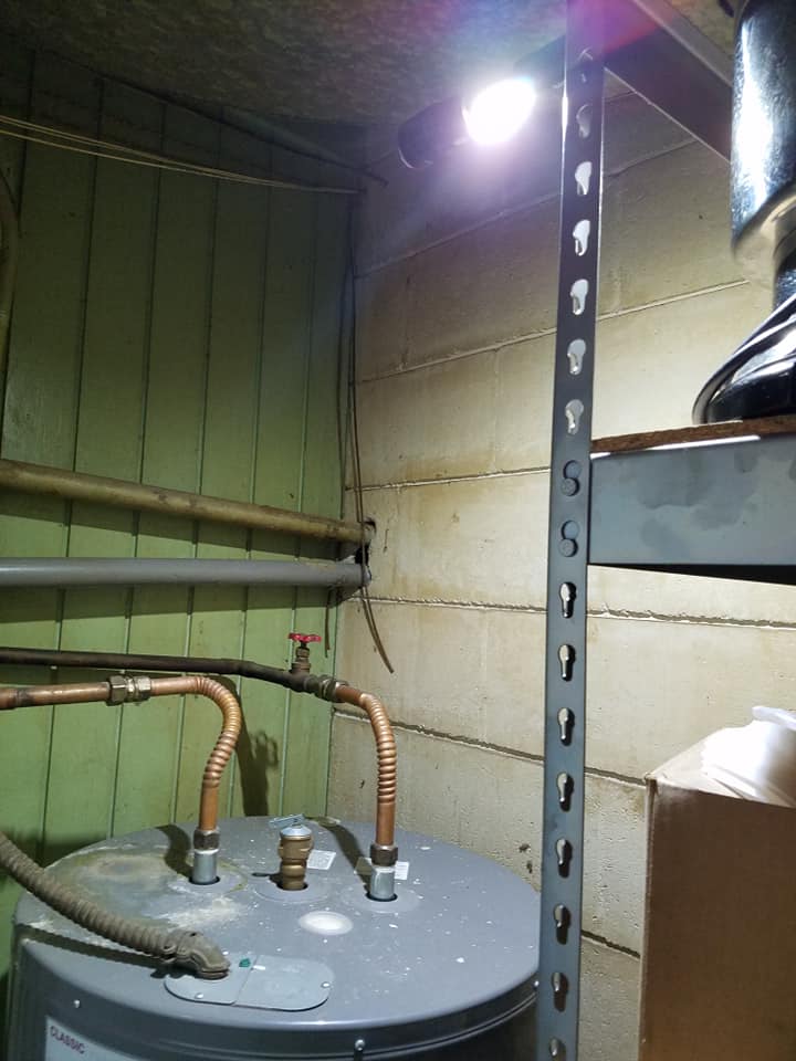 A water heater is sitting under a light in a basement
