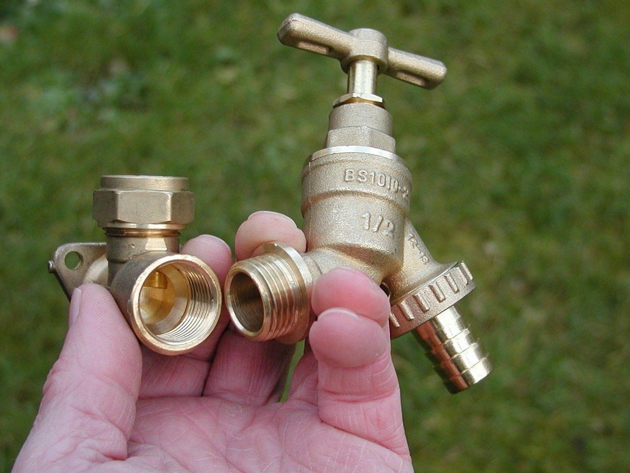 A person is holding two brass faucets in their hand.