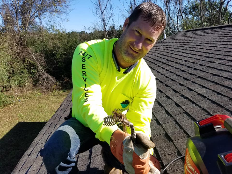 A man in a neon yellow shirt is kneeling on a roof holding a snake.