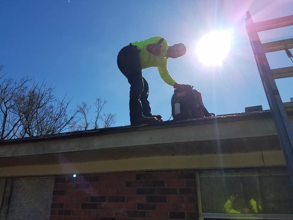 A man is standing on top of a roof with a backpack.