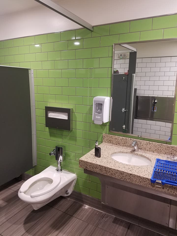 A bathroom with green tiles , a toilet , sink and mirror.