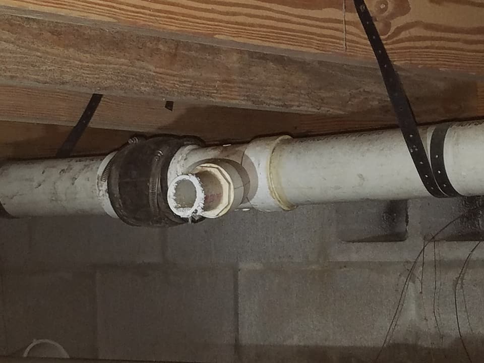 A close up of a pipe under a wooden ceiling in a basement.