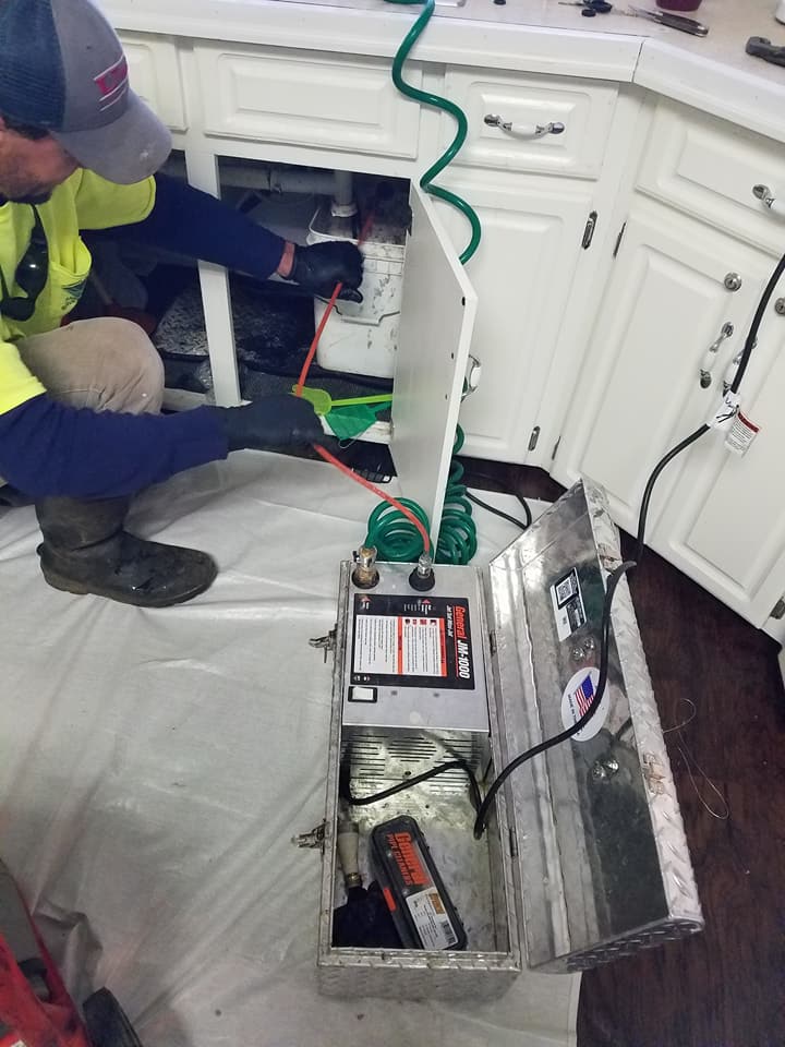 A man is working on a drain under a sink in a kitchen.