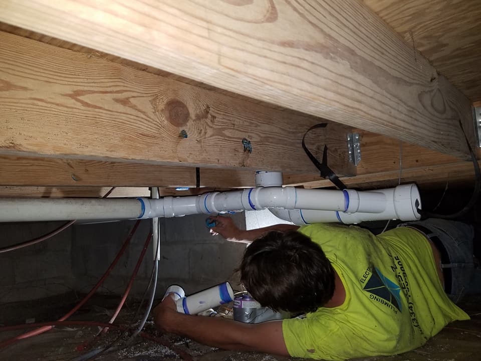 A man is laying on the floor under a house fixing pipes.