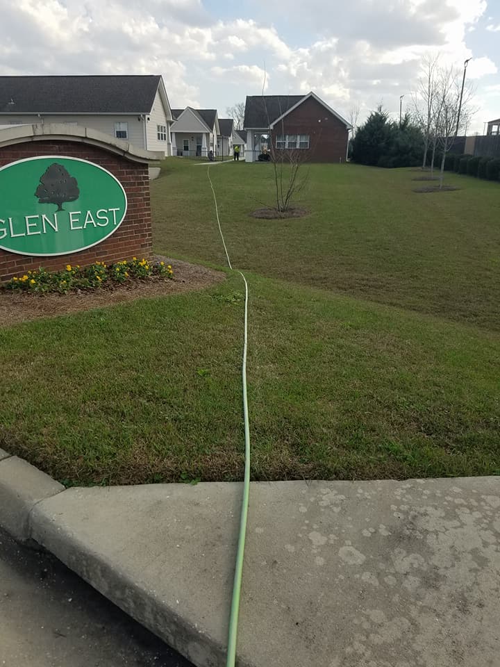 A green hose is laying on the sidewalk in front of a sign that says glen east.