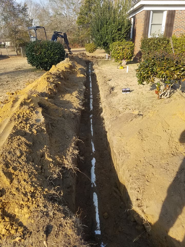 A pipe is being installed in the dirt in front of a house.