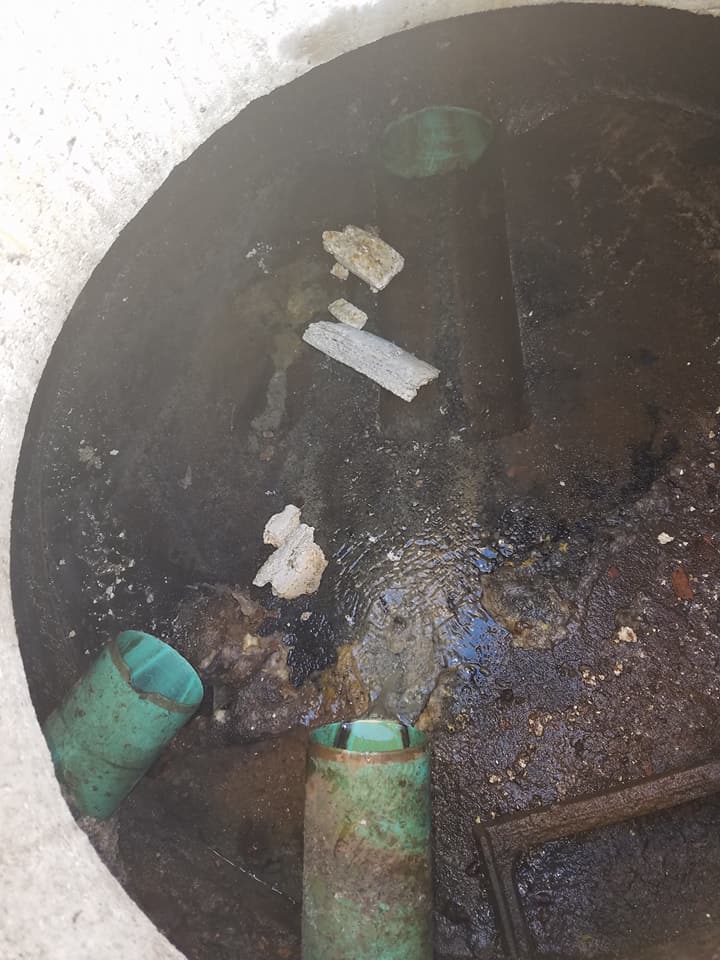 A manhole cover filled with dirty water and pipes.