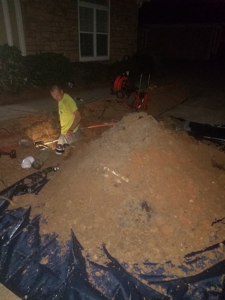 A man is working on a pile of dirt in front of a house at night.
