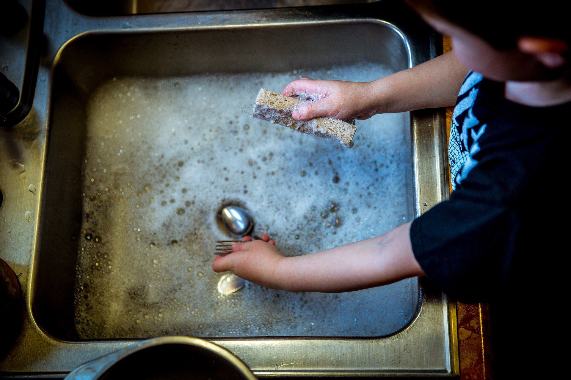 A young boy is washing dishes in a kitchen sink.
