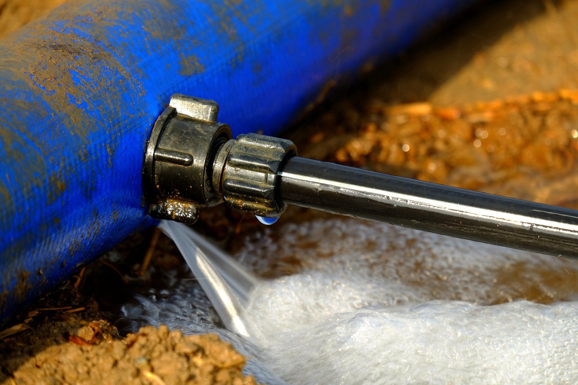 A blue pipe is bursting and water is coming out of it.