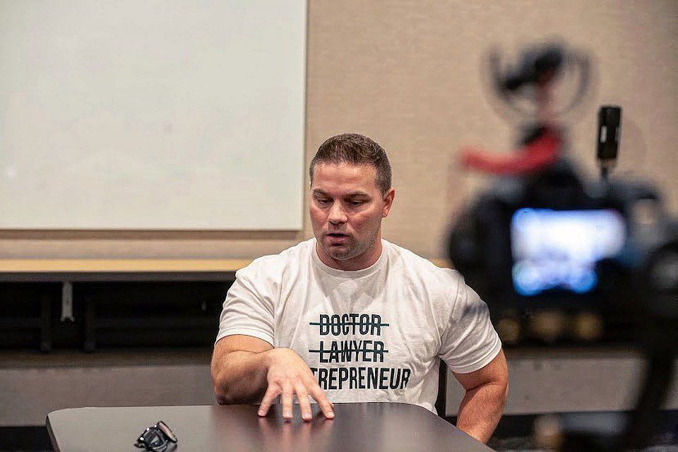 A man is sitting at a table in front of a camera.