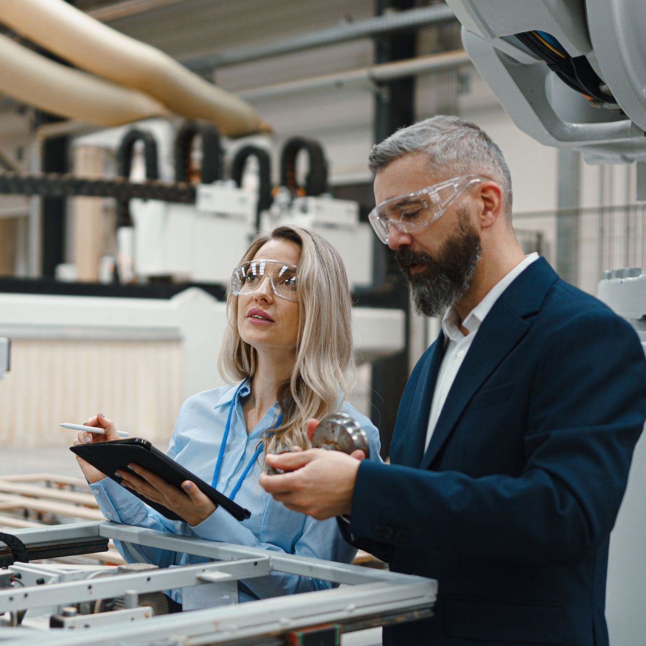 A man and a woman are looking at a tablet in a factory.