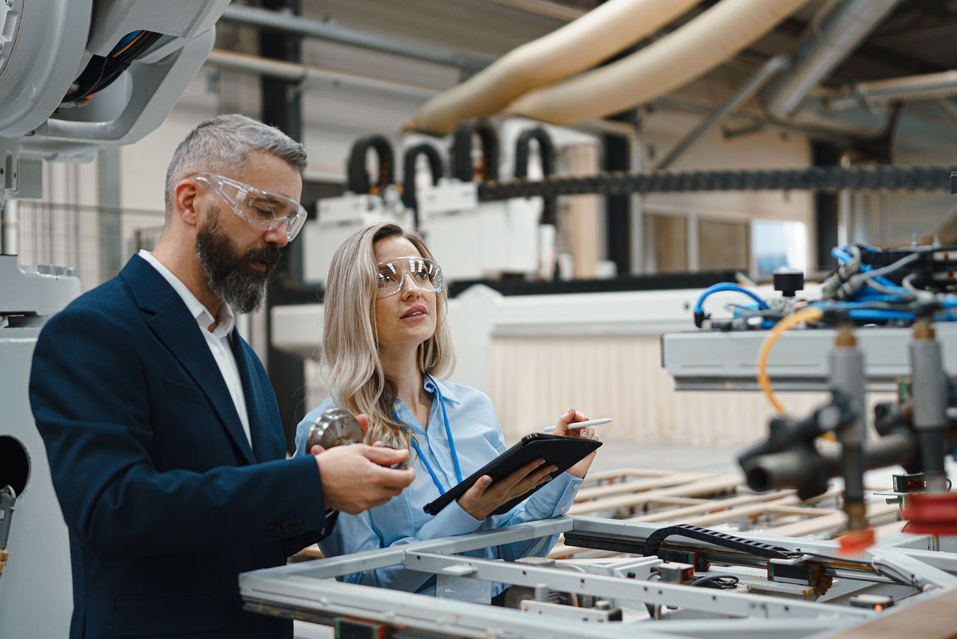 A man and a woman are looking at a tablet in a factory.