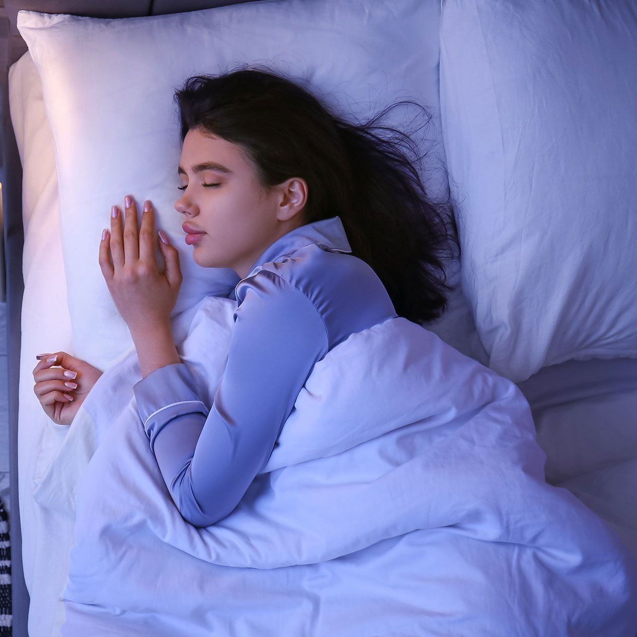 A woman is sleeping in a bed with white sheets and pillows