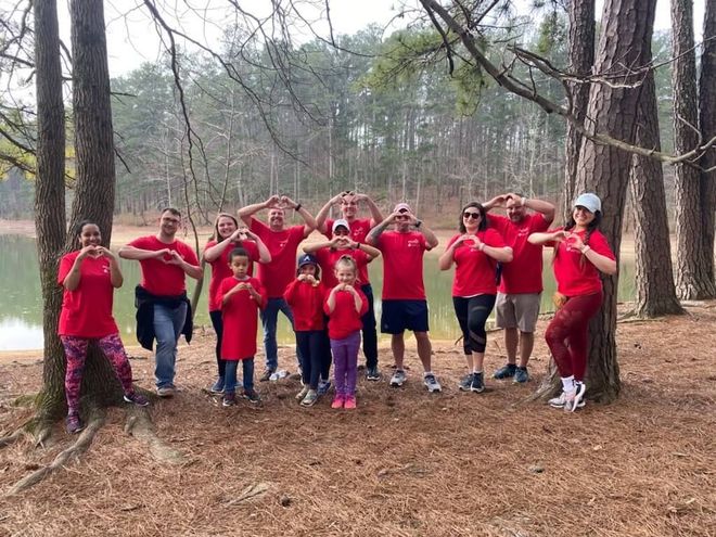 A group of people in red shirts are posing for a picture in the woods.