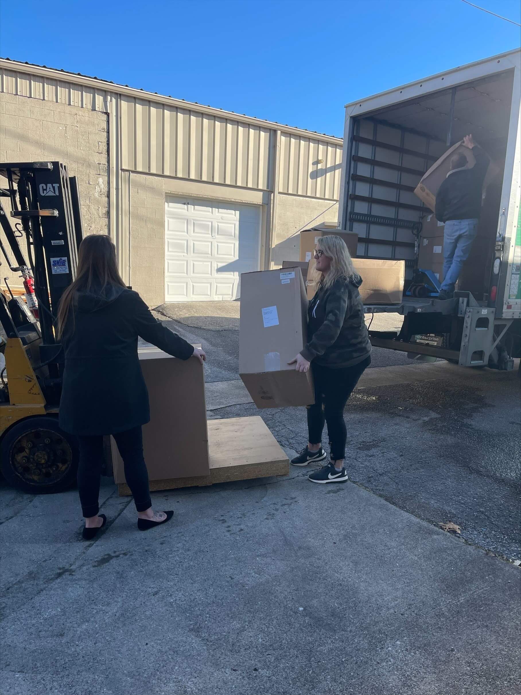 Two women are loading boxes into a truck with a forklift.