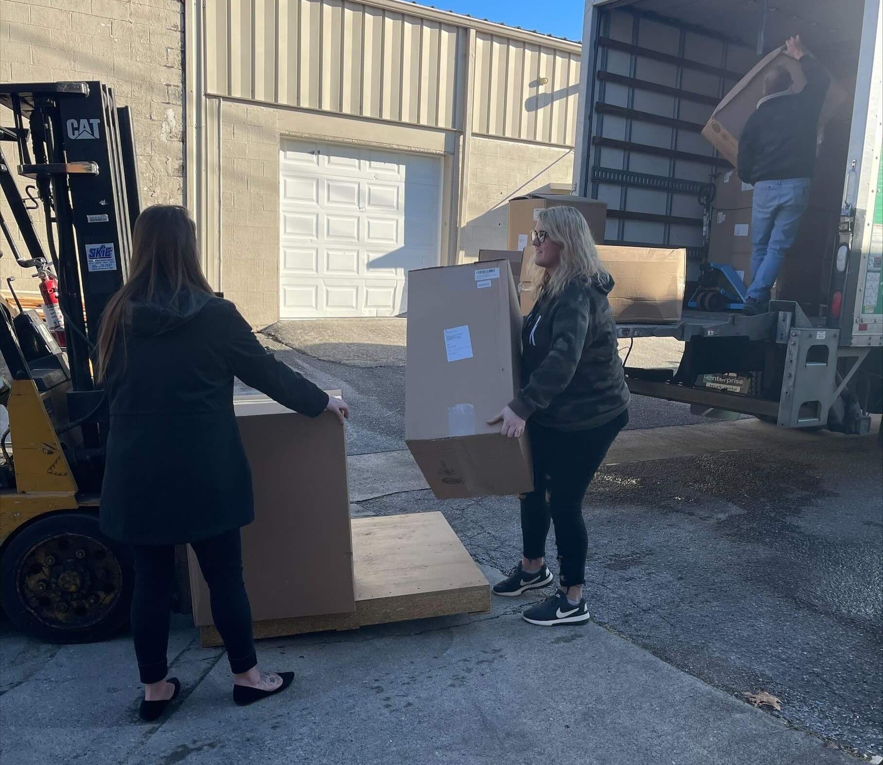 Two women are loading boxes into a truck with a forklift.