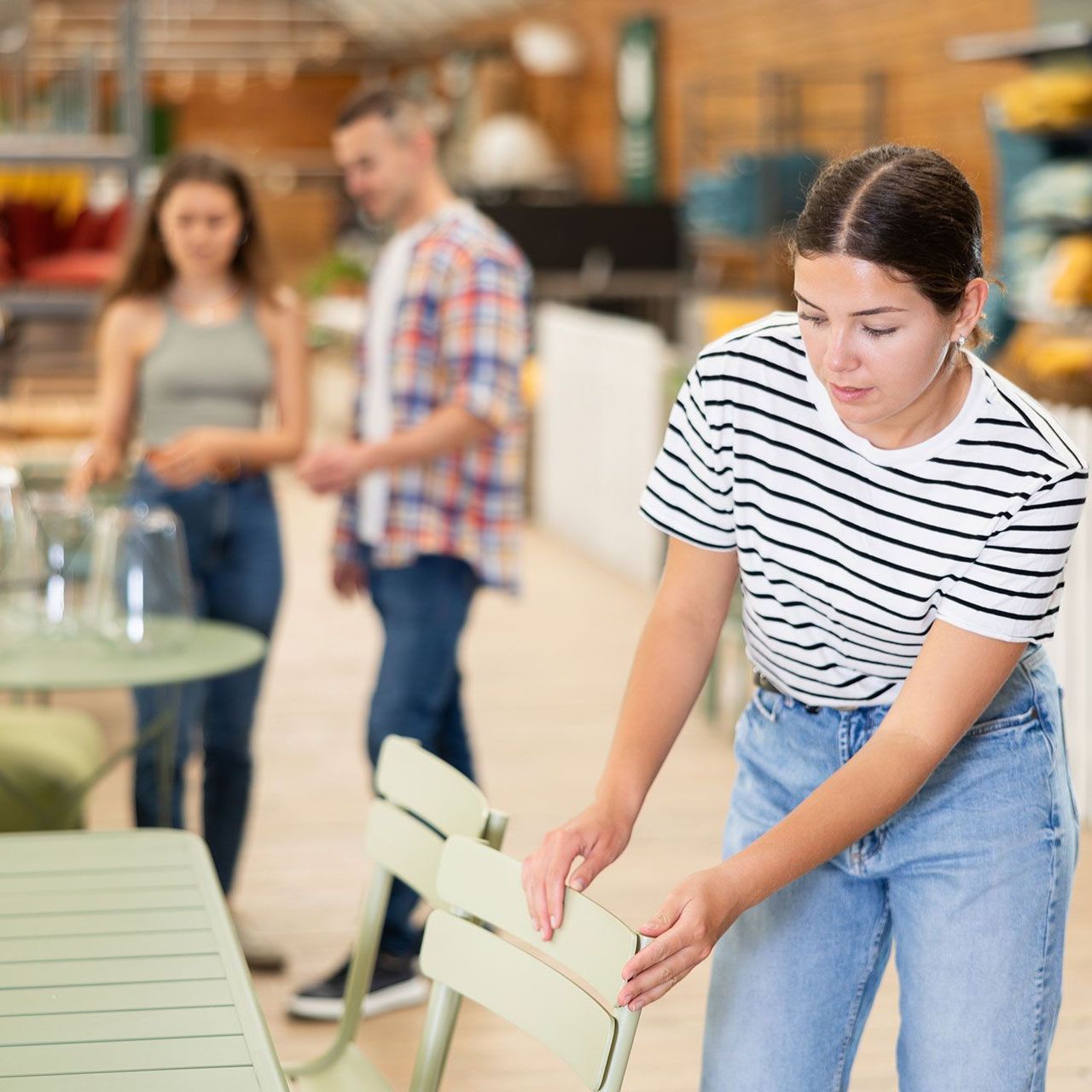 A woman in a striped shirt is putting a chair on a table.