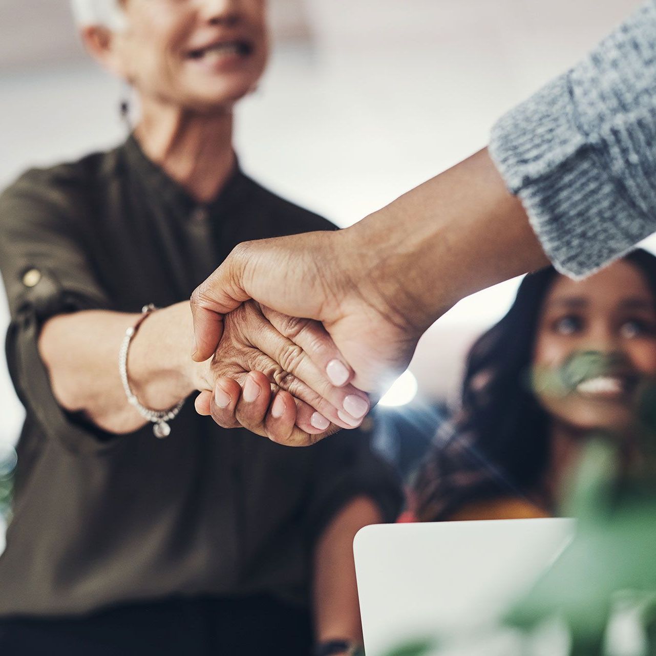 A man and a woman are shaking hands in front of a laptop.