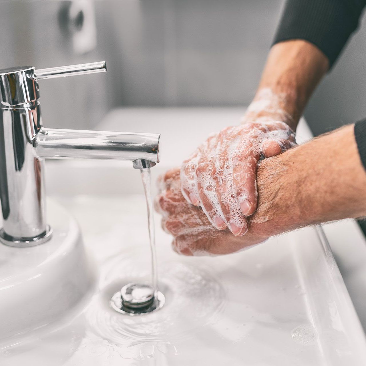 A person is washing their hands in a bathroom sink.