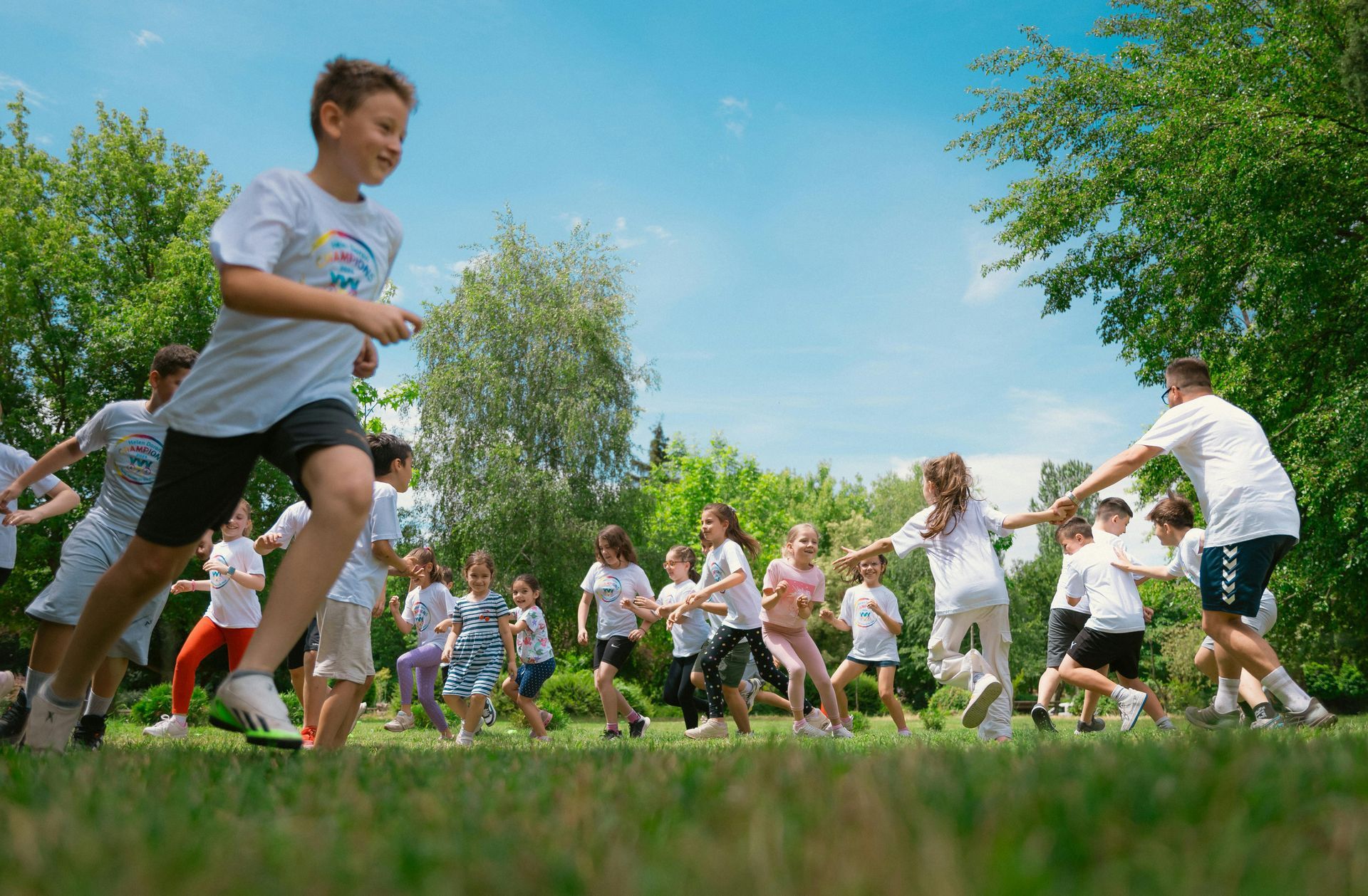 Children running in a grassy park during a group race under a blue sky