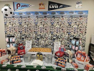 A table with a lot of food on it in front of a wall with a picture of a stadium.